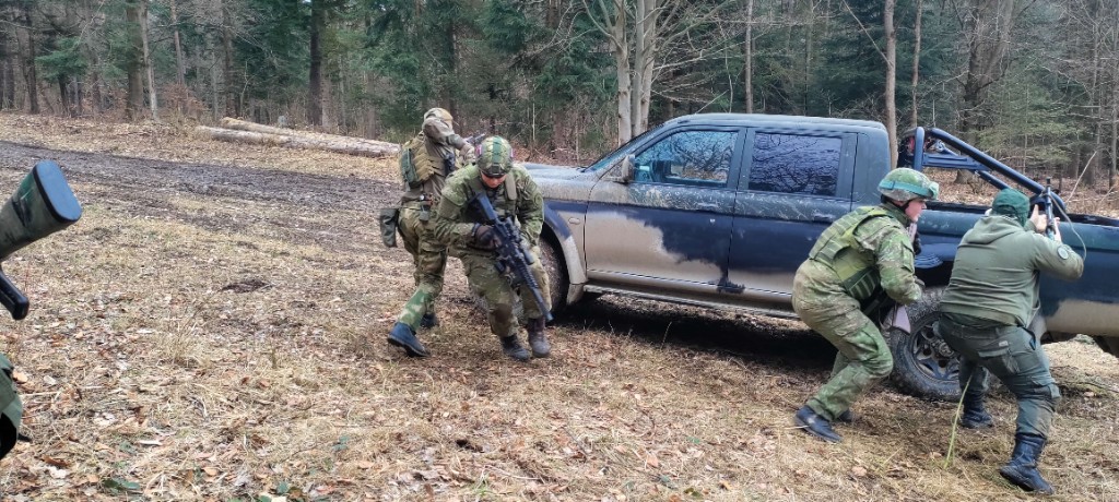 Účastníci v taktickom výstroji pri vozidle v lese